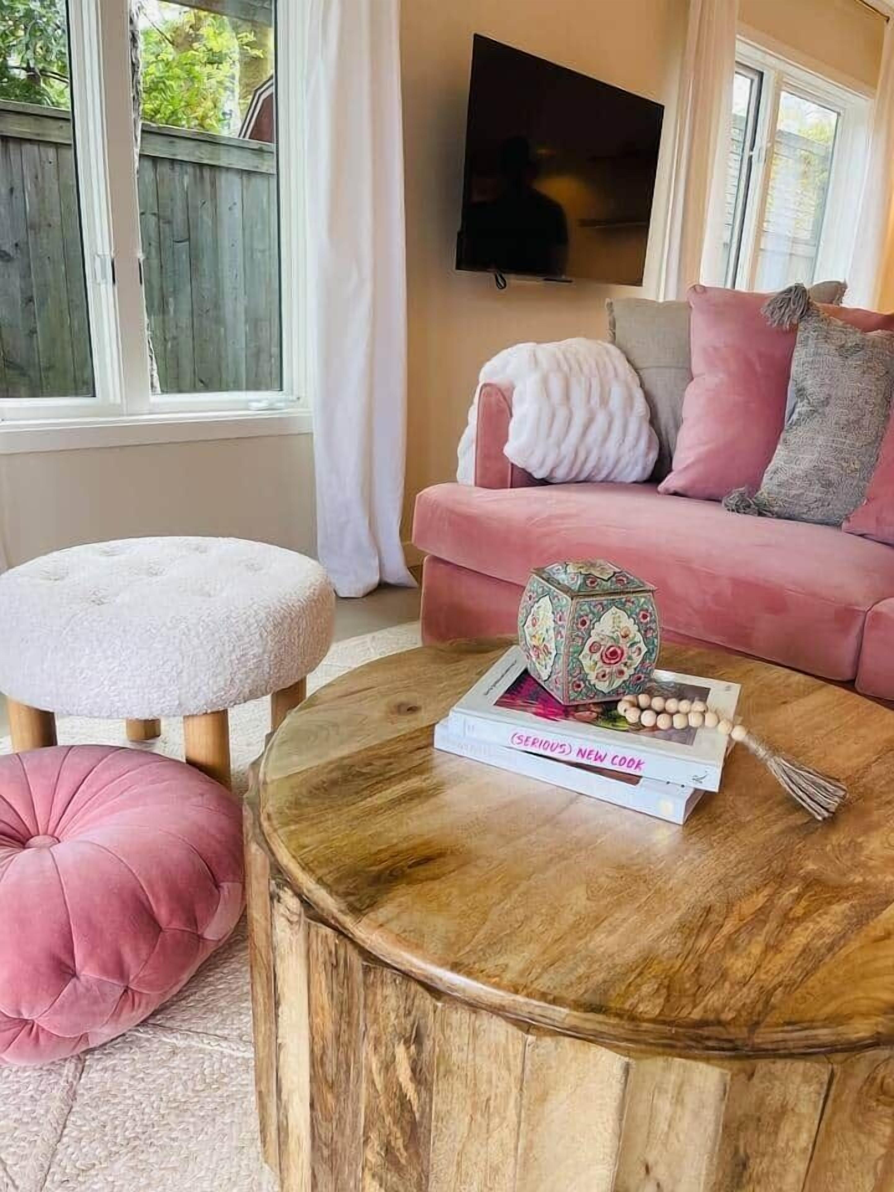 A cozy living room with a round wooden coffee table, a pink sofa, and a white ottoman.