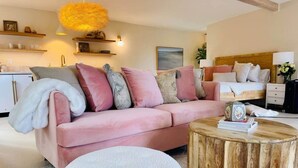 Un salon moderne avec un canapé rose, une table basse ronde en bois et un pouf blanc.