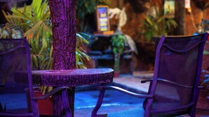 An outdoor seating area with a thatched umbrella, chairs, and a small table. - Arenal Hostel Resort (La Fortuna)