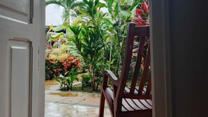 An open door leading to a tiled patio with a wooden rocking chair and various tropical plants. - Arenal Hostel Resort (La Fortuna)