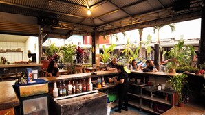 A bar area with a counter, shelves with bottles, and a refrigerator. - Arenal Hostel Resort (La Fortuna)