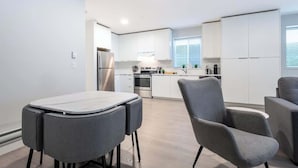 Een moderne keuken met witte kasten, een roestvrijstalen koelkast, en een eethoek met een tafel en stoelen.