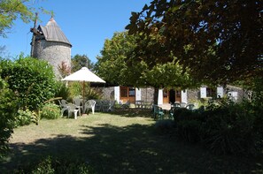 Kivestä rakennettu rakennus, jossa on torni, ja sen ympärillä on vehreää kasvillisuutta sekä ulkotiloihin sijoitettuja istuimia.