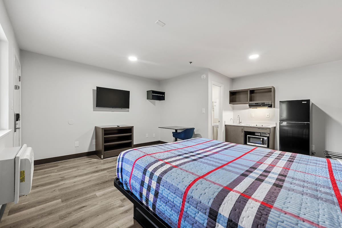 A modern hotel room with a large bed, a flat-screen TV, a microwave, a refrigerator, and a small kitchenette.