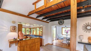 A kitchen with wooden cabinets, a large island, and a dining area with a table and chairs. - Picturesque and Comfy Escape with Waterfall View (Garden Bay)