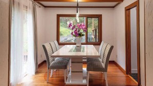 A dining area with a table, four chairs, a vase with flowers, a window with a view, and wooden flooring. - Picturesque and Comfy Escape with Waterfall View (Garden Bay)