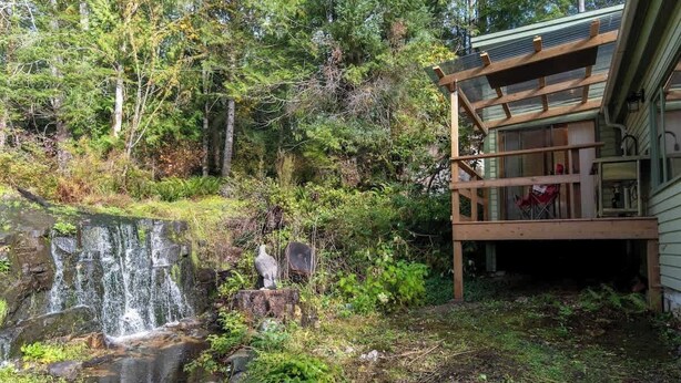 A waterfall, a wooden deck, and a building surrounded by trees. - Picturesque and Comfy Escape with Waterfall View (Garden Bay)