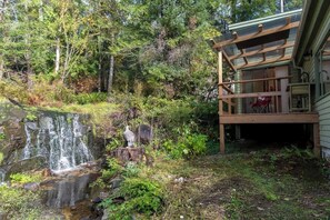 A waterfall, a wooden deck, and a building surrounded by trees. - Picturesque and Comfy Escape with Waterfall View (Garden Bay)