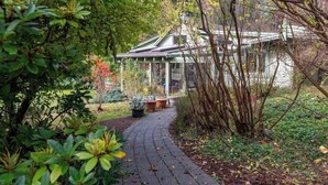 A garden pathway leading to a conservatory with a glass roof, surrounded by lush greenery. - Picturesque and Comfy Escape with Waterfall View (Garden Bay)