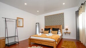 A bedroom with a wooden bed, a mirror, a wardrobe, a patterned wall, and a small bedside table with a lamp. - GuestReady - Villa Isla (Ponta Delgada)
