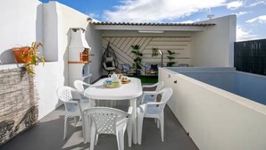 A rooftop terrace with a white table and chairs, a hanging chair, and a small barbecue area. - GuestReady - Villa Isla (Ponta Delgada)