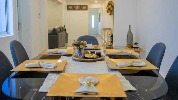 A dining area with a glass table set for six, each place setting with a folded napkin and a small vase of flowers. - GuestReady - Villa Isla (Ponta Delgada)