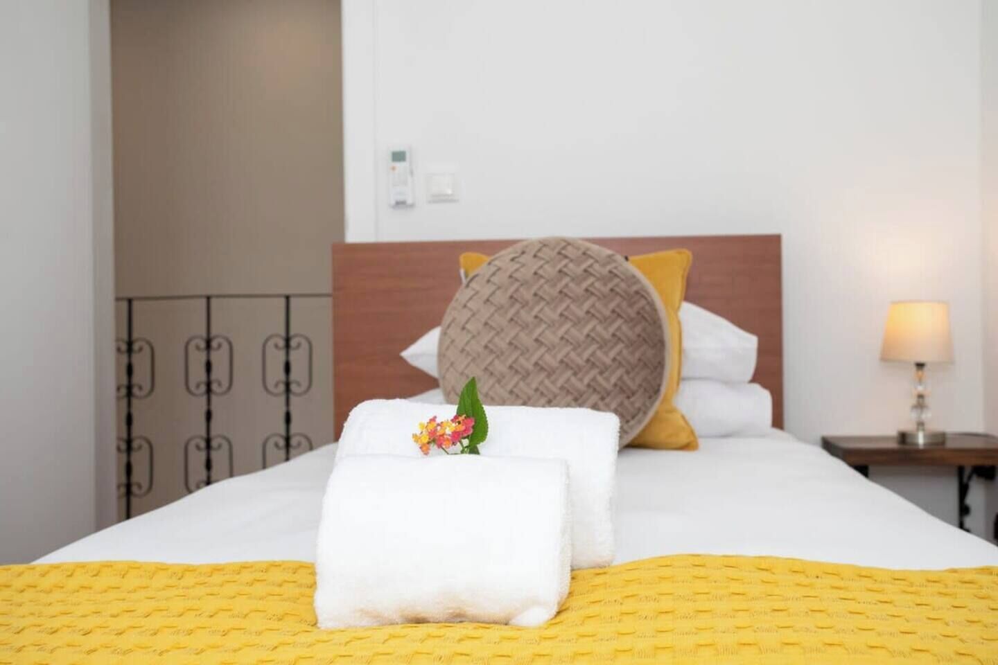 A neatly made bed with a yellow bedspread, white pillows, and a brown woven pillow.