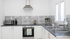 A modern kitchen with white cabinets, a stainless steel range hood, a microwave, and a dish drying rack. - GuestReady - Villa Isla (Ponta Delgada)