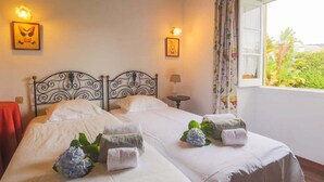 A double bed with white linens, two wall-mounted lamps, and a window with floral curtains.