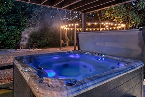 A hot tub with a wooden exterior, surrounded by a covered patio area with string lights.