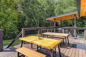 Eine Terrasse im Freien mit Holztischen und -bänken, umgeben von einem Metallgeländer und Bäumen.