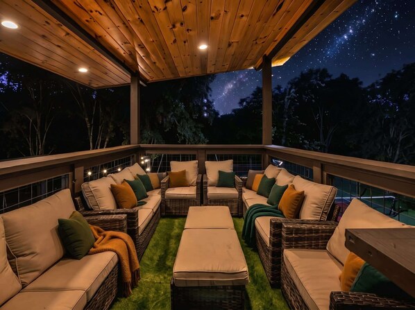 An outdoor deck with wicker furniture and cushions, a wooden ceiling, and a night sky view.
