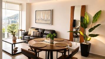 A modern living room with a leather sofa, a round wooden dining table with woven placemats, and a large potted plant.