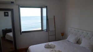 A hotel room with a large window overlooking the sea, a neatly made bed, a bedside table, and a mirror. - GuestReady - Casa da Boa Viagem (Ribeira Grande)