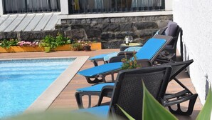 A poolside area with lounge chairs and a table, surrounded by potted plants and a stone wall. - GuestReady - Casa da Boa Viagem (Ribeira Grande)