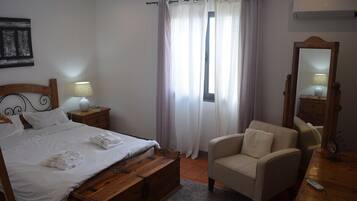 Ein Schlafzimmer mit Bett, Nachttischen, einem Sessel, einem Spiegel und einem Fenster mit Vorhängen.