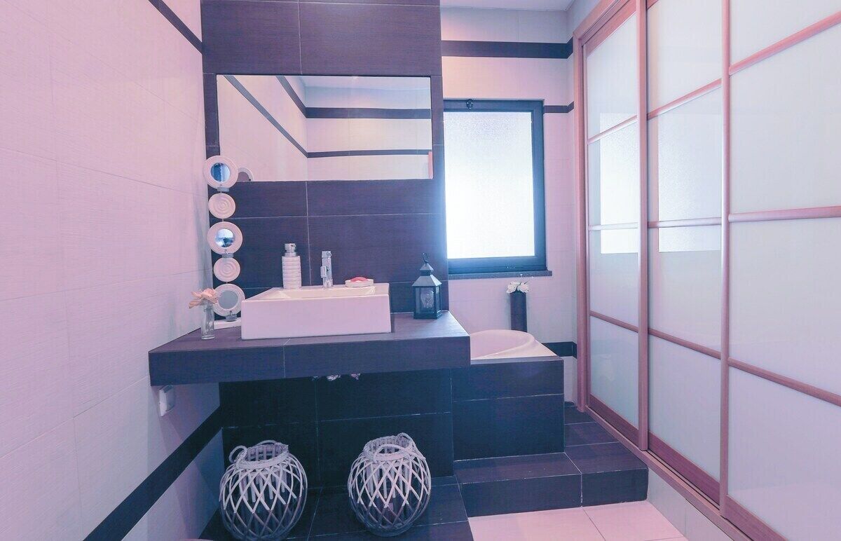 Une salle de bain moderne avec un meuble-lavabo foncé, un grand miroir et une fenêtre laissant entrer la lumière naturelle.