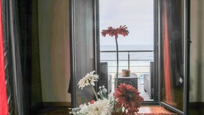 A room with a view of the ocean through a large window, a potted plant, and a table with a chair. - GuestReady - Casa da Boa Viagem (Ribeira Grande)