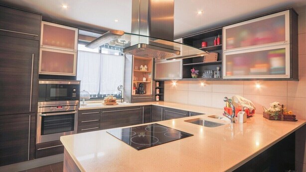 A modern kitchen with built-in appliances, a central island, and a large window providing natural light. - GuestReady - Casa da Boa Viagem (Ribeira Grande)
