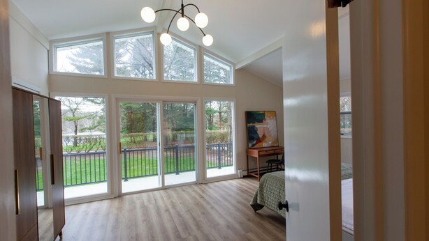A spacious room with large windows, a wooden floor, a desk, and a bed. - Luxurious, fully renovated 5 bedroom home great indoor & outdoor living spaces (Newton)