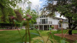 A two-story house with a balcony, surrounded by a well-maintained lawn and trees. - Luxurious, fully renovated 5 bedroom home great indoor & outdoor living spaces (Newton)