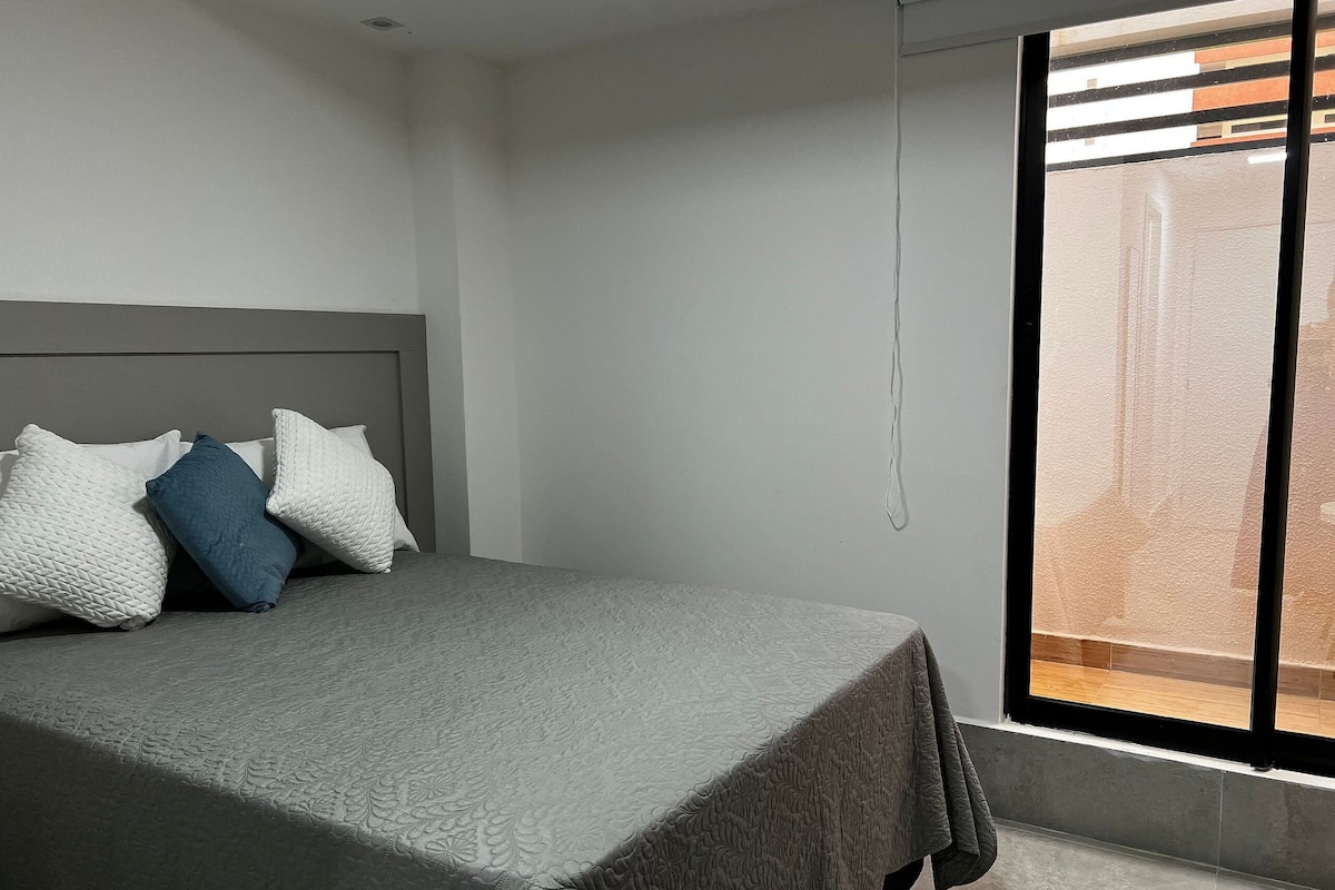 A bedroom with a bed, pillows, and a window.