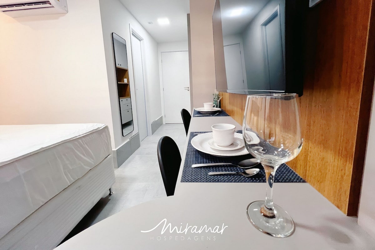 A hotel room with a bed, a dining table with a wine glass, and a TV mounted on the wall.