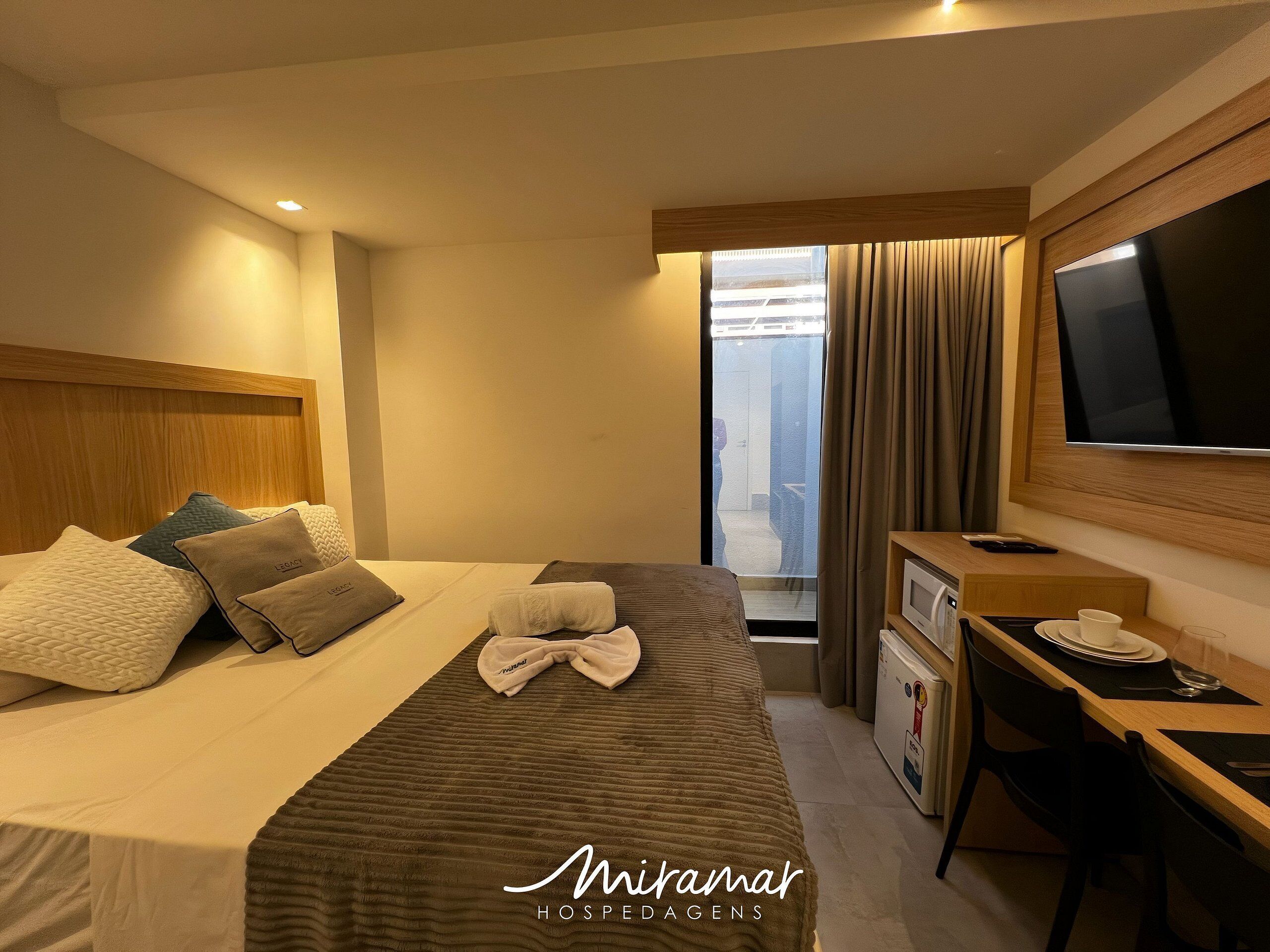 Ein Hotelzimmer mit Bett, Schreibtisch, Fernseher und einem Fenster mit Vorhängen.