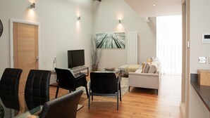A modern living room with a flat-screen TV, a sofa, and a dining area with chairs.