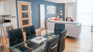 A modern living room with a glass dining table, grey sofa, and a blue accent wall.