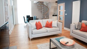 A modern living room with a grey sofa, a coffee table, and a dining area with a glass table and chairs.