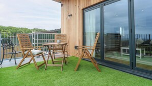 Un terrazzo in legno con tavolo e sedie, una porta vetrata e vista sulla campagna circostante.