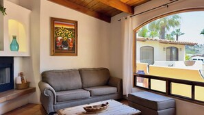 A cozy living room with a sofa, a wooden coffee table, and a large window with a view of a building and palm trees.