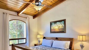 Una cama de madera con colcha a rayas, dos lámparas de noche, un cuadro enmarcado en la pared y una ventana con cortinas.