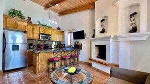 A modern kitchen with wooden cabinets, a stainless steel refrigerator, and a microwave. There is a dining area with a round glass table and chairs.