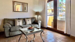 Una sala de estar con sofá, mesa de centro, lámpara y un amplio ventanal con cortinas.