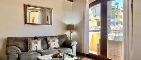 Ein Wohnzimmer mit einer Couch, einem Couchtisch, einer Lampe und einem großen Fenster mit Vorhängen.