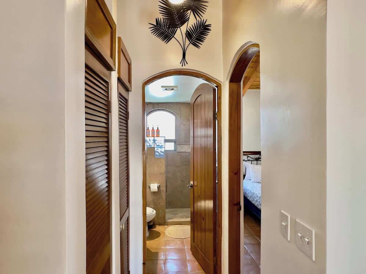 Pasillo que conduce a un baño con ducha e inodoro, puertas de madera y un ventilador de techo.