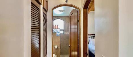Pasillo que conduce a un baño con ducha e inodoro, puertas de madera y un ventilador de techo.