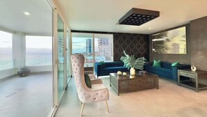 A modern living room with a glass partition, a blue sofa, a pink armchair, and a coffee table.