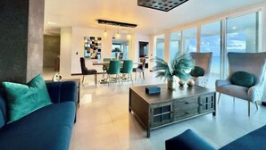 A modern living room with a sofa, armchair, coffee table, and a dining area with chairs and a table.