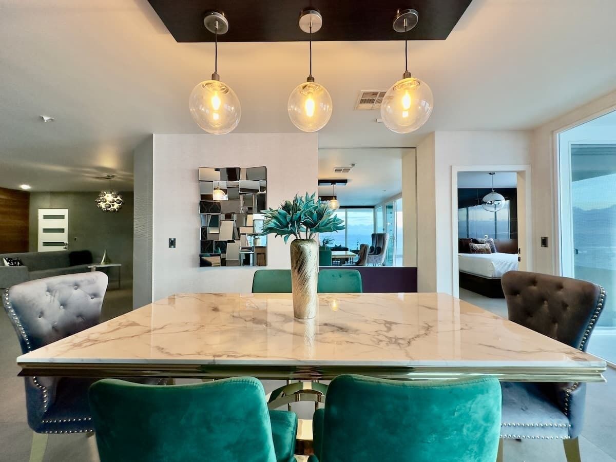 A modern dining area with a marble table, teal chairs, and pendant lighting.