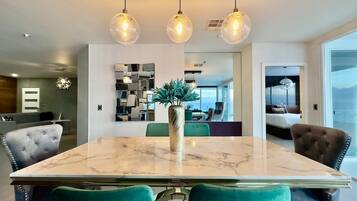 A modern dining area with a marble table, teal chairs, and pendant lighting.