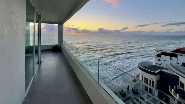 A balcony with a view of the sea and a building across the water.